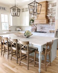 a kitchen with white cabinets and wooden chairs in front of an island table surrounded by hanging lights