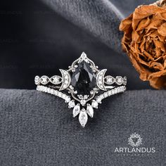 a black diamond ring sitting on top of a piece of cloth next to a rose