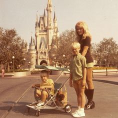 a woman pushing a stroller with two children on it in front of a castle