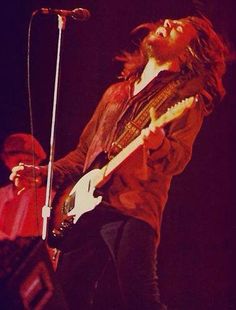 a man with long hair playing an electric guitar in front of a microphone on stage