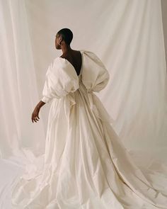 a woman in a white dress is standing on a white background with her hands behind her back