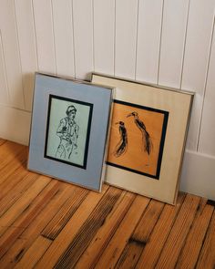 two framed pictures sitting on top of a wooden floor