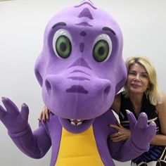 two women pose for a photo with a large purple dinosaur mascot in front of them