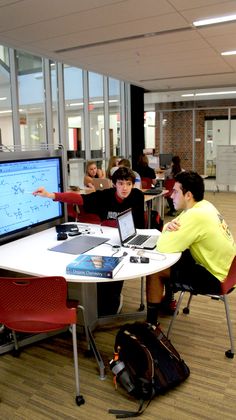 two boys sitting at a table with laptops in front of them and one boy pointing to the screen