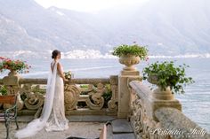 a woman in a wedding dress standing on a balcony looking at the water and mountains