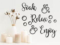 some candles are sitting on a table next to a vase and wall decal that says relax enjoy