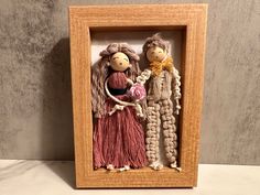 two dolls are in a wooden frame with yarn on the sides and one is holding a ball of yarn