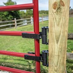 a red gate with two black latches on it and a wooden fence in the background