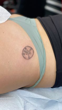 a woman's stomach with a small sand dollar tattoo on her left side ribcage