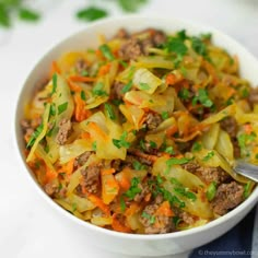 a white bowl filled with meat and vegetables on top of a table next to a spoon