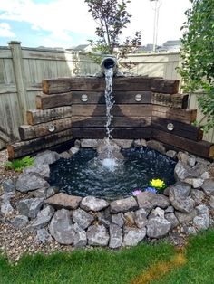 a water fountain in the middle of a garden with rocks around it and a wooden fence behind it