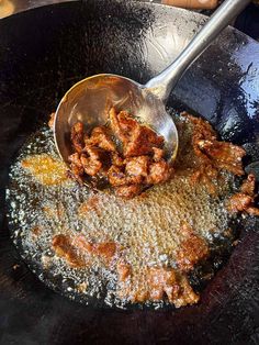 a frying pan filled with fried meat being stirred by a ladle over it