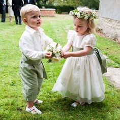 two young children dressed in formal clothing holding hands and looking at each other while standing on grass