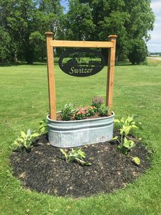 a sign that is in the grass near some bushes and flowers, with a tub full of plants