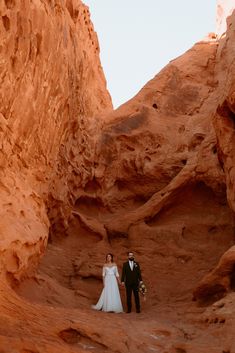 a man and woman standing in the middle of a canyon with red rocks on either side