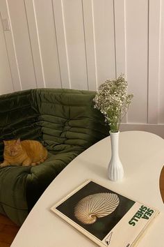 an orange cat sitting on top of a green couch next to a white table with a book