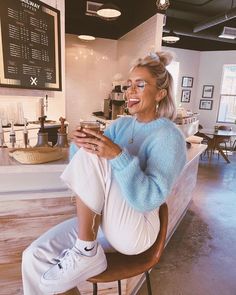 a woman sitting in a chair at a coffee shop looking at her cell phone and smiling