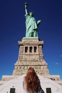 a woman standing in front of the statue of liberty