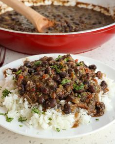 a white plate topped with rice and beans next to a red casserole dish