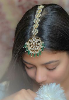 a woman is holding a flower and wearing a head piece with jewels on it's side