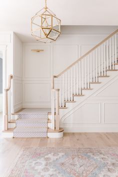 an empty room with stairs and rugs on the floor in front of a chandelier