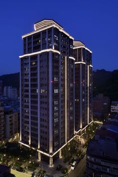 the building is lit up at night with lights on it's sides and cars parked in front