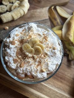 a dessert with bananas and whipped cream in it on a wooden table next to sliced bananas