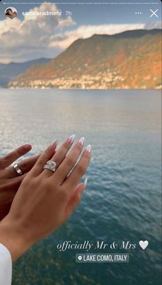 two hands holding each other over water with mountains in the background and sky above them