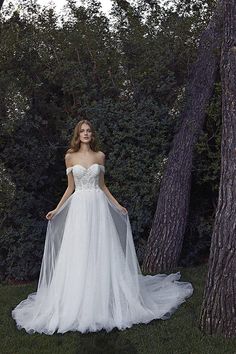 a woman in a wedding dress standing next to some trees