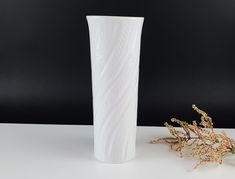 a white vase sitting on top of a table next to a small flower pot and dried plant