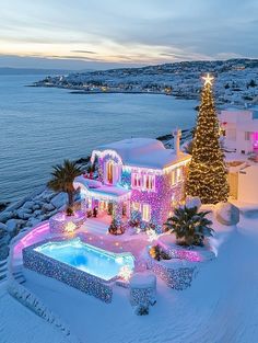 a large house covered in christmas lights next to the ocean with a lit up tree