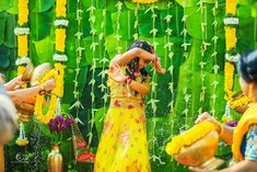 a woman in a yellow dress standing next to a green wall covered in flowers and greenery