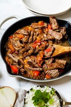 a skillet filled with meat and vegetables on top of a table next to rice