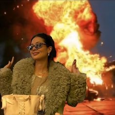 a woman wearing glasses and a fur coat is standing in front of a large explosion