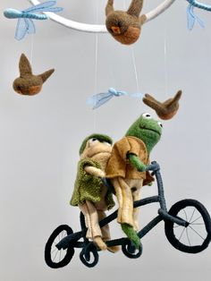 two stuffed animals are riding on a bicycle with birds hanging from the strings above them