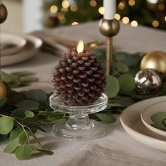 a pine cone sitting on top of a glass plate next to candles and greenery