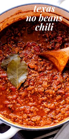 a large pot filled with chili and a wooden spoon in it, on top of a table