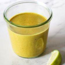 a small glass jar filled with yellow liquid next to a lime