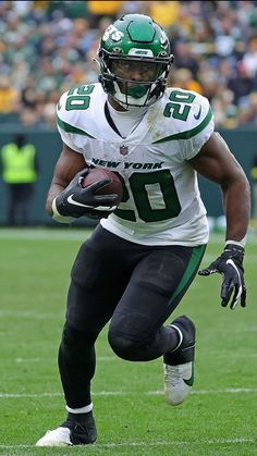 a football player running with the ball in his hand and wearing a green helmet on