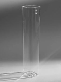 a tall clear glass vase sitting on top of a white table next to a shadow