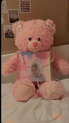 a pink teddy bear sitting on top of a bed next to a box with a photo