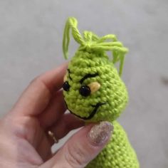 a hand holding a small green crocheted animal