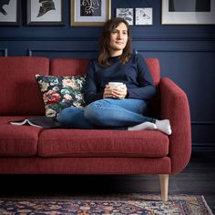 a woman sitting on a red couch holding a coffee cup in her hand and looking at the camera