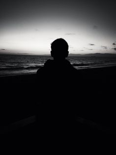 the silhouette of a person sitting on a bench looking out at the ocean in front of them