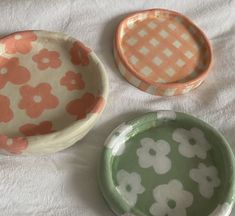 three plates with flower designs on them sitting on a white cloth covered tablecloth, one has an orange and the other is green