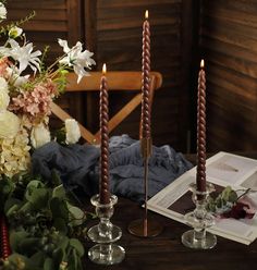 there are three candles on the table with flowers in front of it and an open book