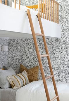 a bunk bed with a ladder next to it and pillows on the bottom shelf below