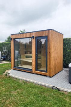 a small wooden building with glass doors on the front and side, sitting in a grassy area