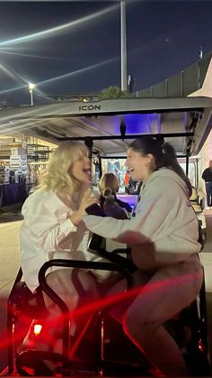 two women sitting in a golf cart talking to each other while one woman holds her hand out