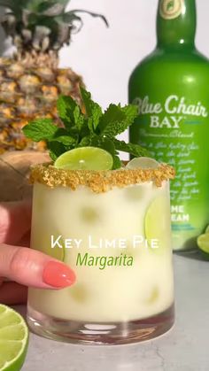 a person is holding a margarita with limes on the rim and a bottle in the background